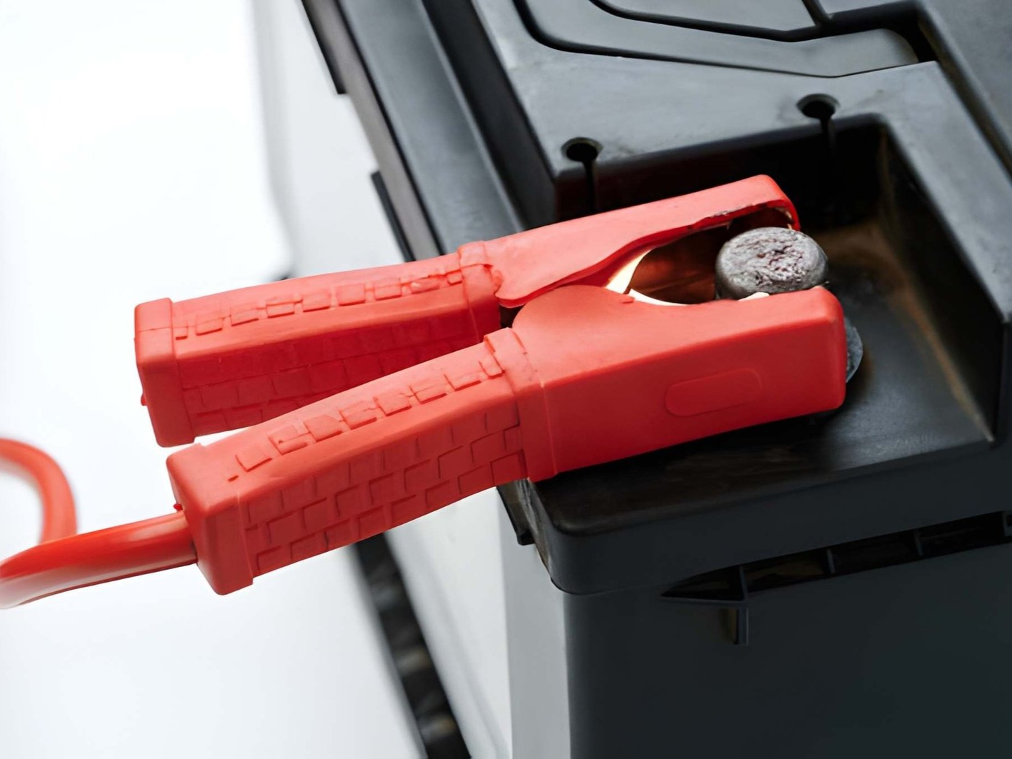 The image shows a red jumper cable clamp attached