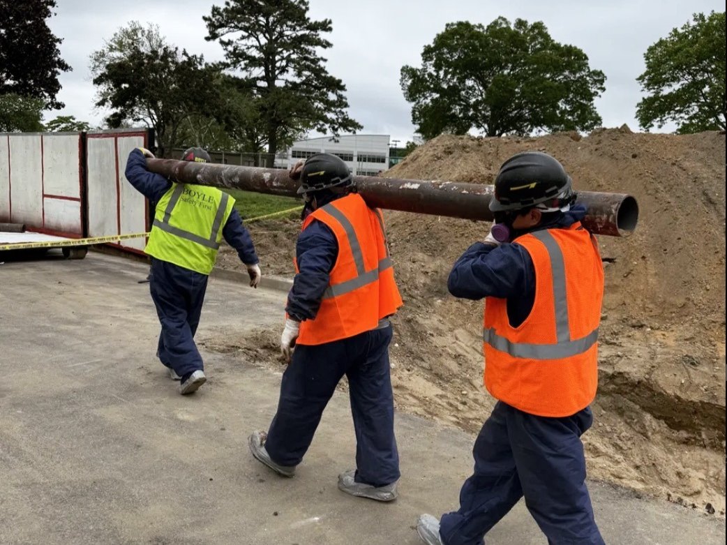Workers in hard hats and safety vests carrying equipment