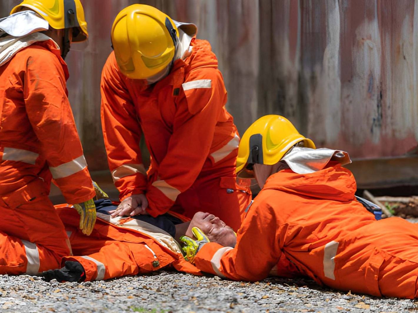 Three workers in orange jumpsuits and yellow hard hats